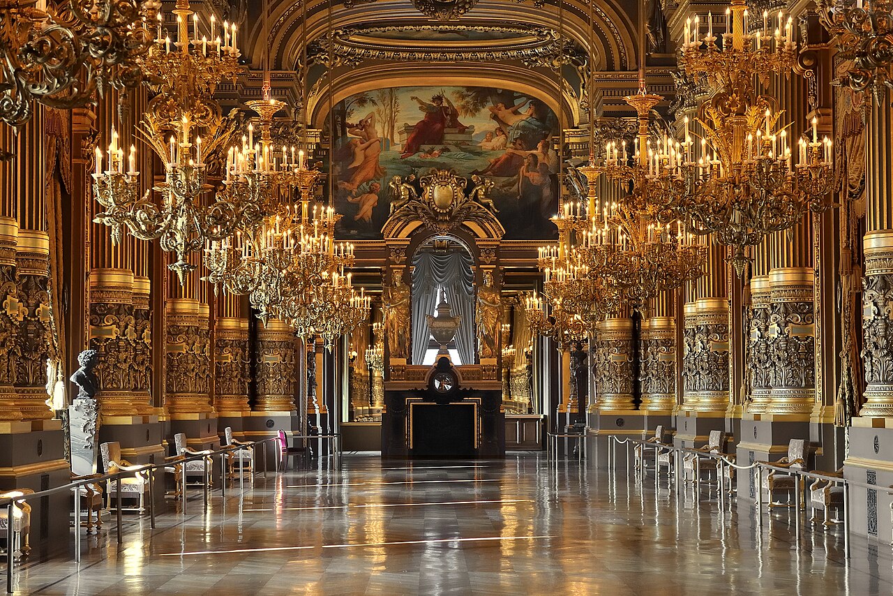 Grand foyer interior of the Palais Garnier opera house in Paris with ornate gilt walls and chandeliers
