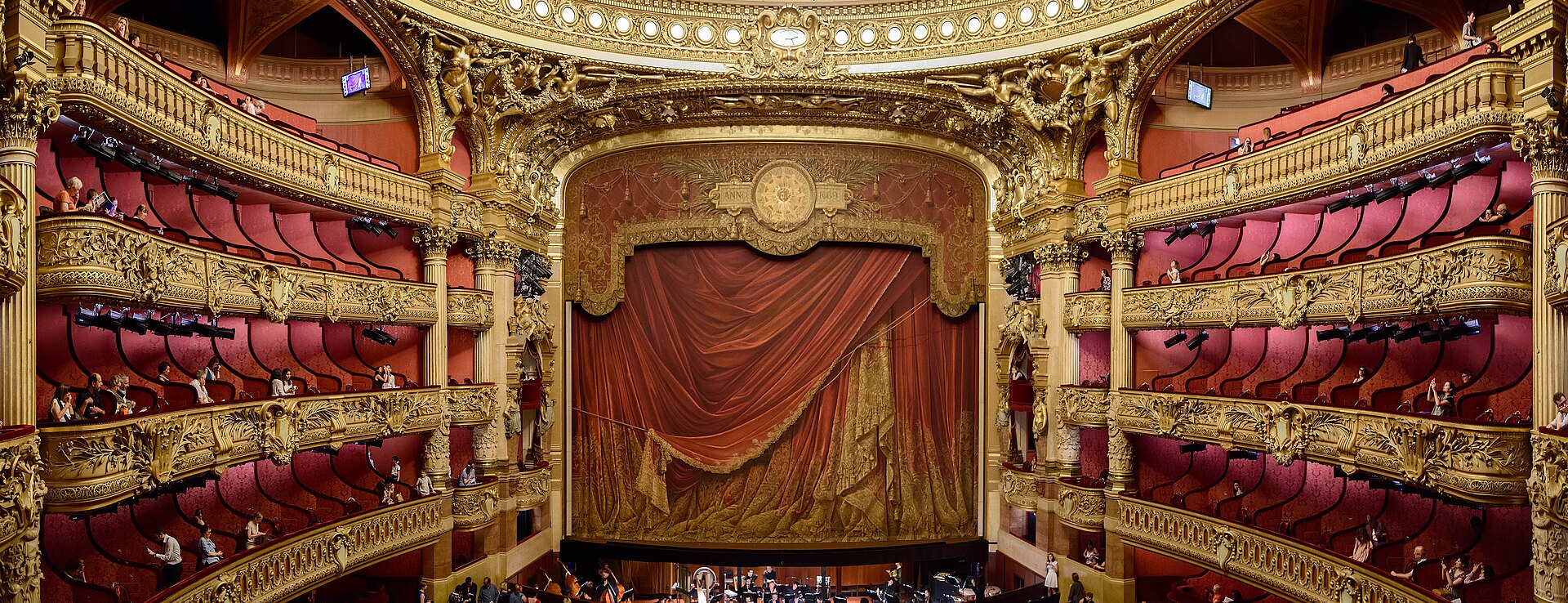 Panoramic view of the red and gold auditorium of the Palais Garnier in Paris, with its tiers of boxes and chandelier