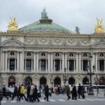 The ornate front facade of the Palais Garnier opera house in Paris with gilded statues on the roof