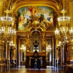 The gilded Grand Foyer of the Palais Garnier opera house in Paris, with chandeliers and a painted ceiling