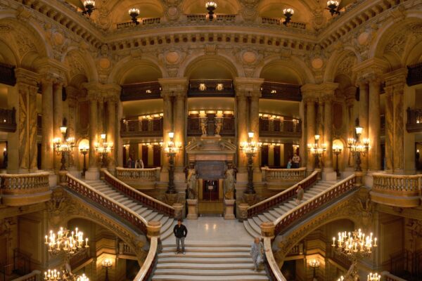 The marble Grand Staircase of the Palais Garnier opera house in Paris, lit by ornate candelabra beneath gilded arches