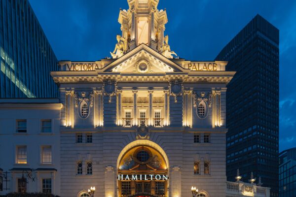 Victoria Palace Theatre in London lit up at night, with HAMILTON displayed above the entrance canopy