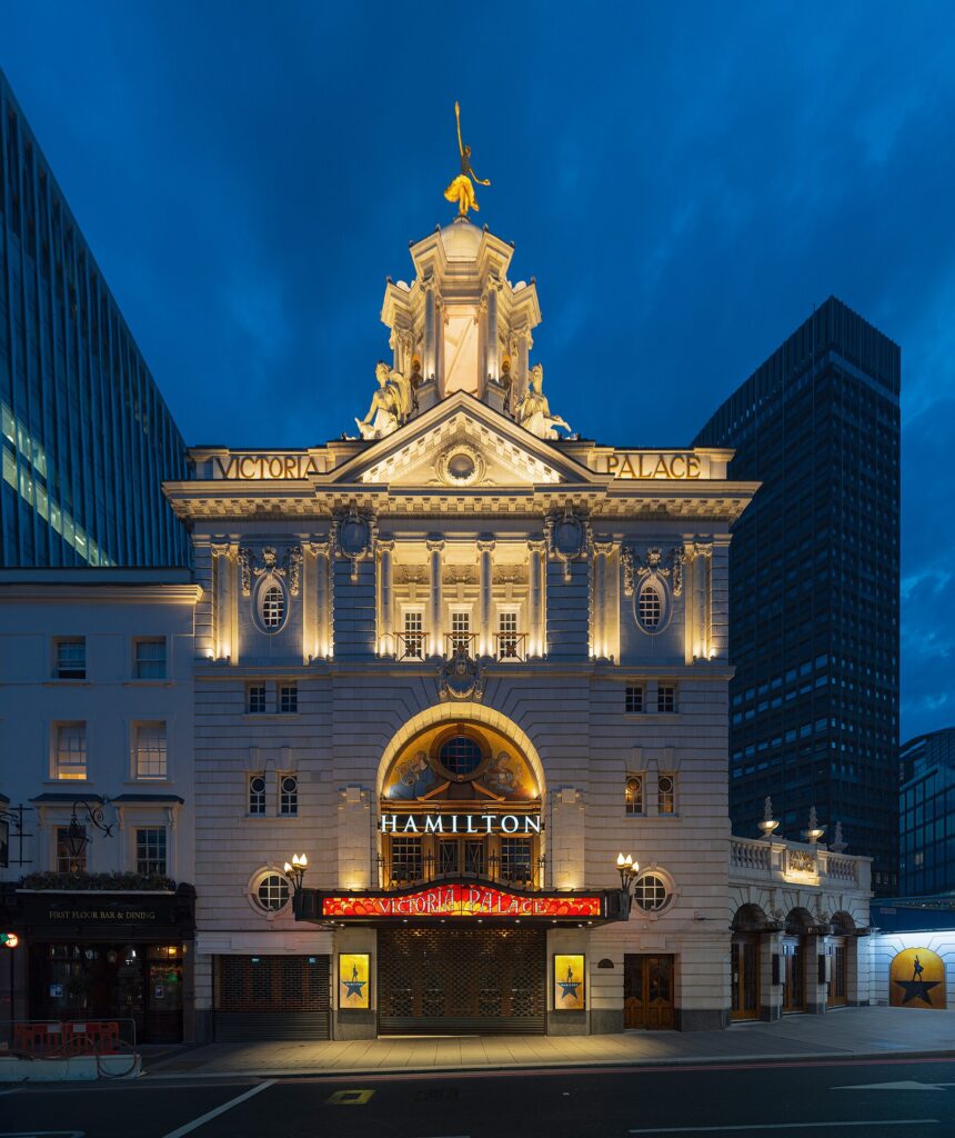 Victoria Palace Theatre in London lit up at night, with HAMILTON displayed above the entrance canopy